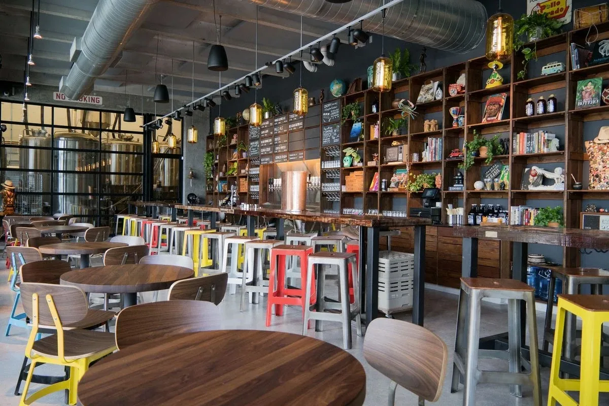 Interior taproom with a long wood bar, stainless brewing tanks, colorful stools and tables at Casa La Rubia, Miami