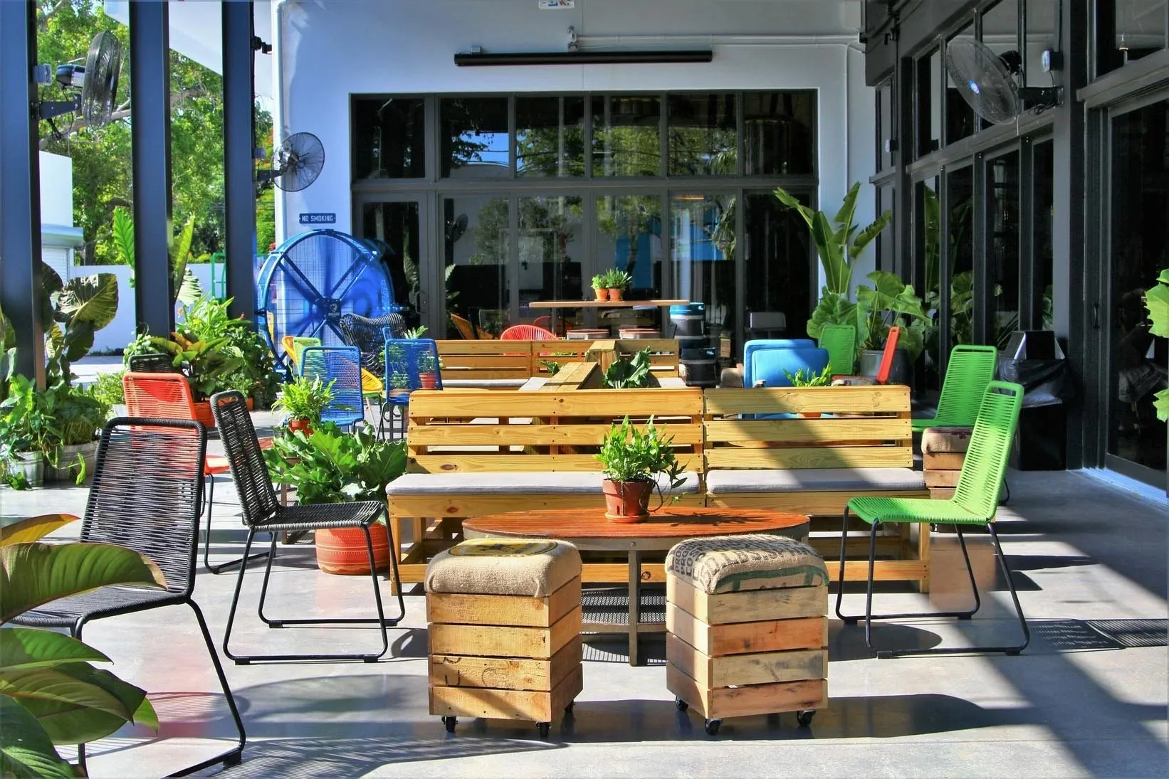 Outdoor covered patio with pallet-wood benches, colorful woven chairs and potted plants at Casa La Rubia, Miami