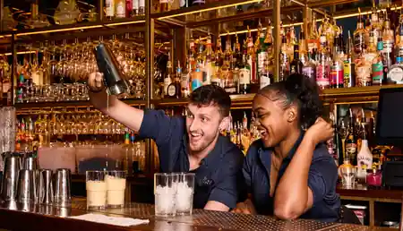 Bartenders mixing cocktails behind the bar at Be At One Liverpool Street with shelves of spirits — salsa, bachata, kizomba venue in London