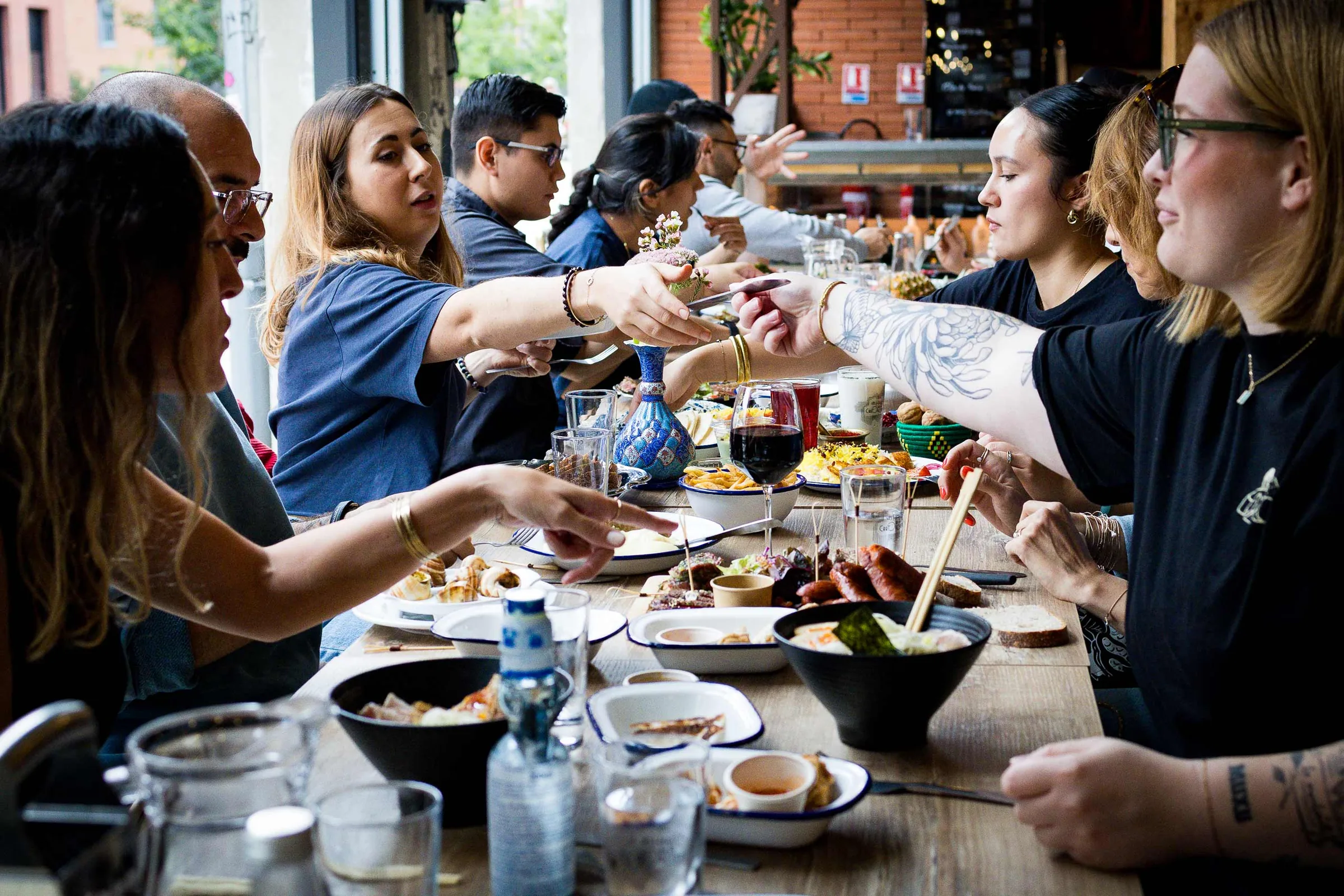 Guests sharing plates of food and drinks along a long communal wooden table inside the food hall at Les Halles de la Cartoucherie, Toulouse.