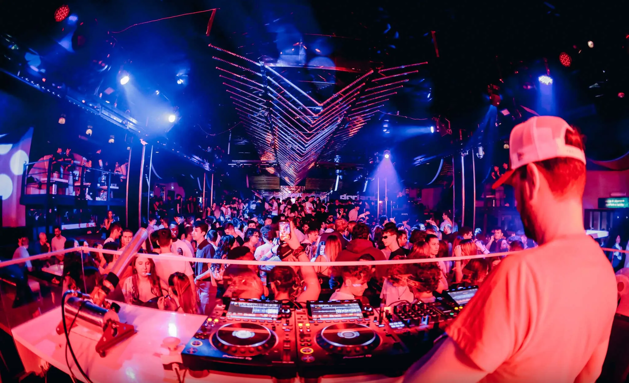 DJ playing to packed dance floor under V-shaped lighting rig at Discoteca Dorian Gray Verona