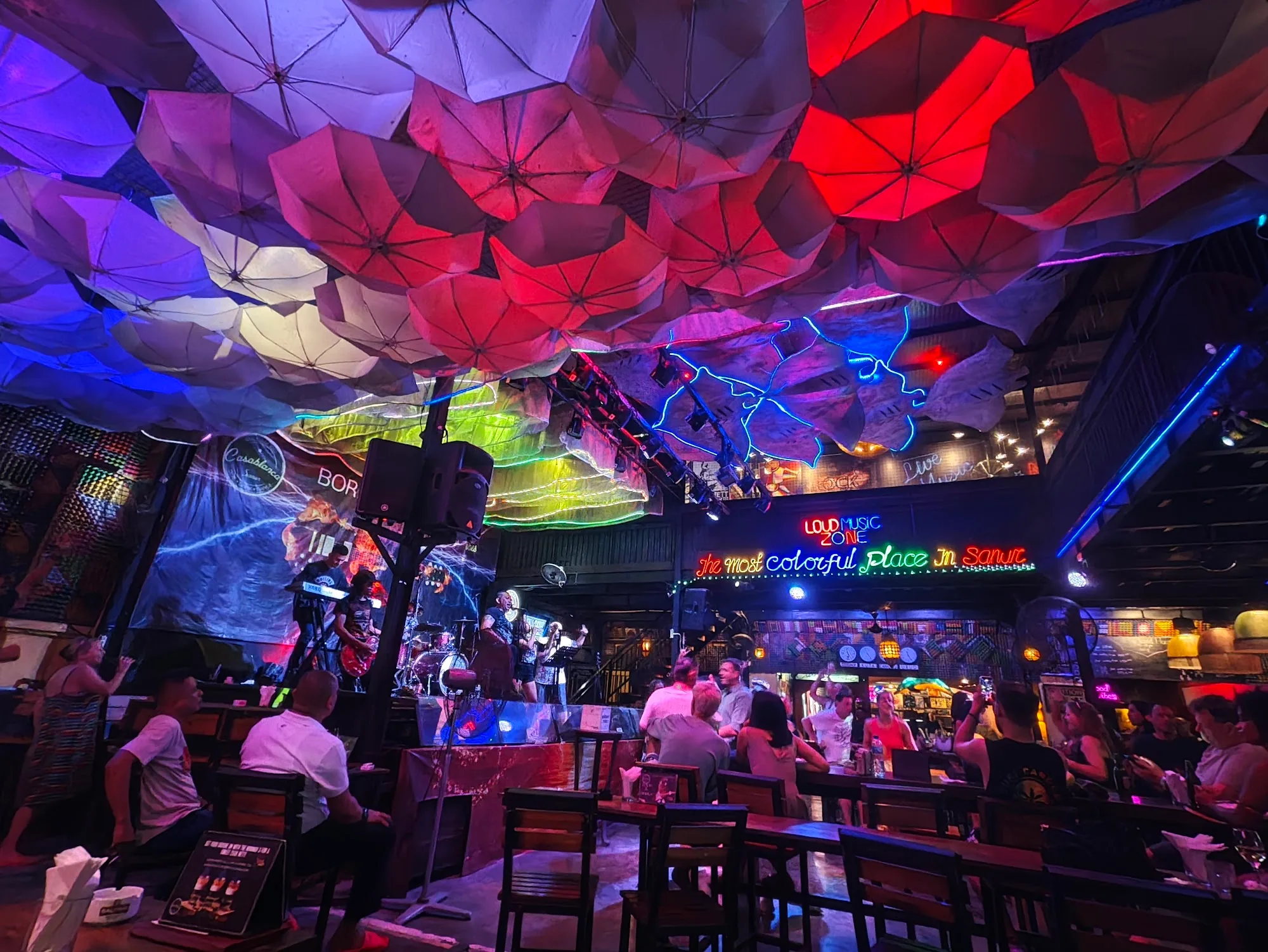 Colorful umbrella ceiling, neon lights and live band with crowd at Bakfickan Bar in Sanur, Bali