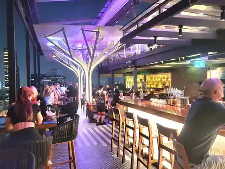 Bar interior with tree columns and guests at Above Eleven rooftop bar, Bangkok — salsa venue in Bangkok