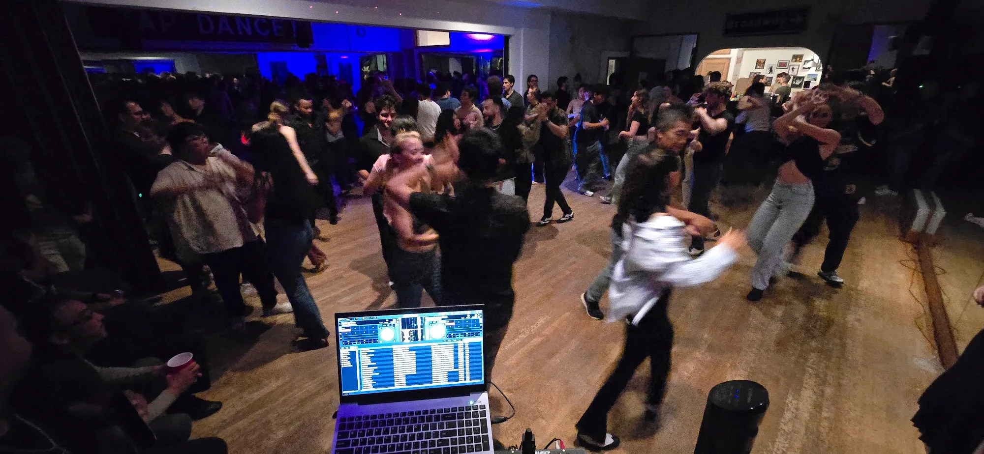 Crowded social dance floor with partner dancers and DJ laptop at The Beat in Berkeley