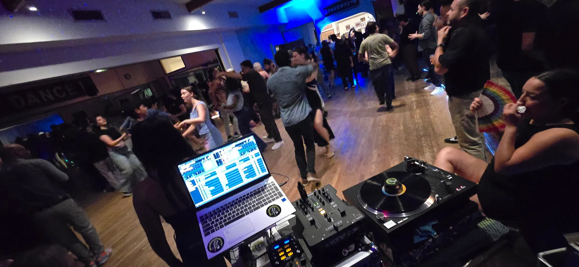 Salsa social with dancers and DJ setup under blue lights at The Beat in Berkeley