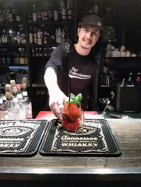 Bartender in branded shirt mixing a cocktail at the bar of Das Wohnzimmer in Wiesbaden, salsa venue in Wiesbaden