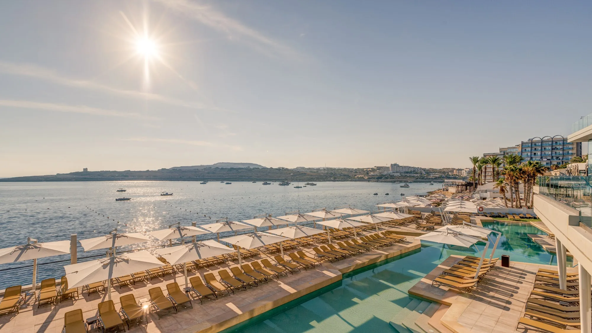 Outdoor pool area with beach and sea at AX Hotels Malta