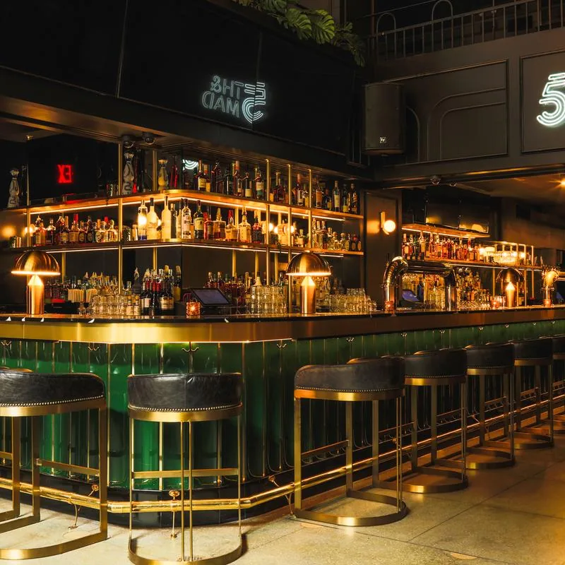 Green and gold cocktail bar with neon 5th & Mad branding, New York