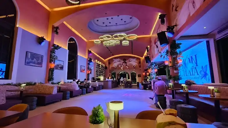 Amavi Bali dance venue interior at night with colorful purple and blue lighting, open dance floor surrounded by lounge seating, and a large screen displaying a Bachata dance event