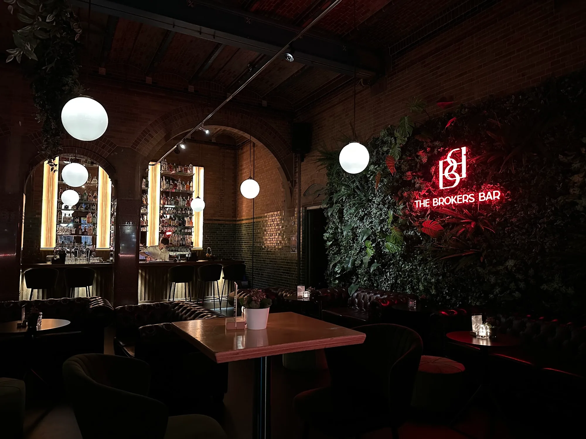 Neon 'The Brokers Bar' sign lit in red with lush green wall in Amsterdam