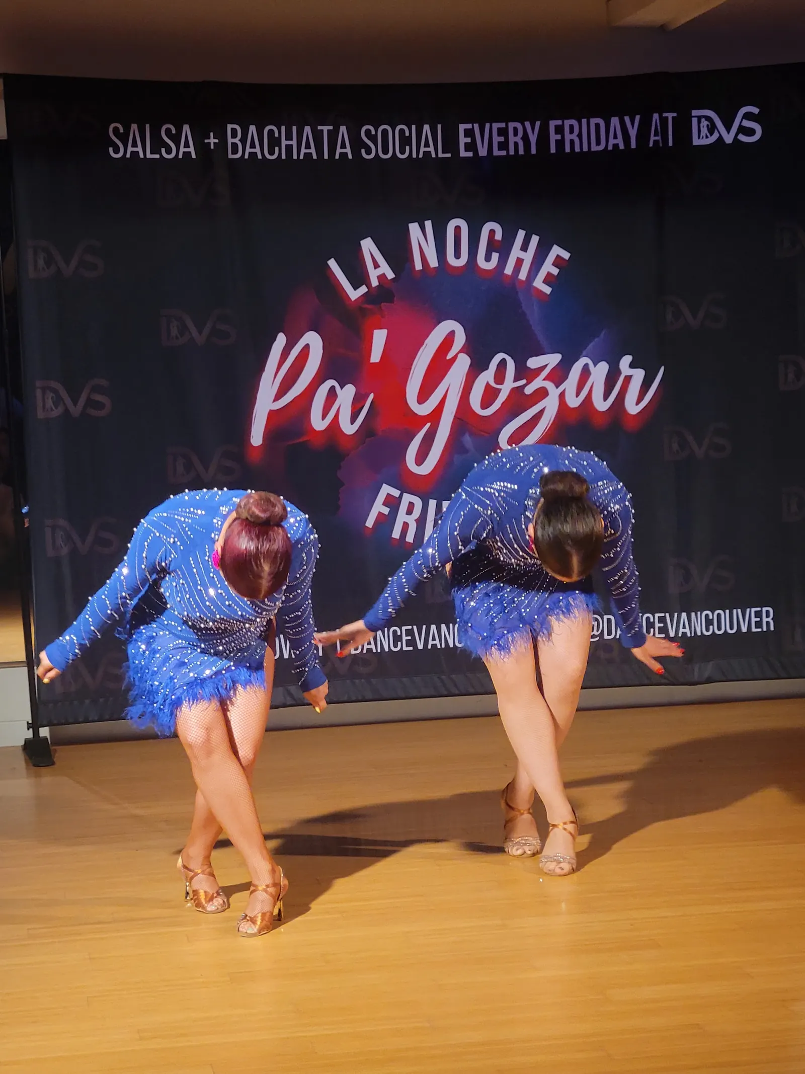 Two performers dancing in front of the DVS Friday social banner on the studio floor