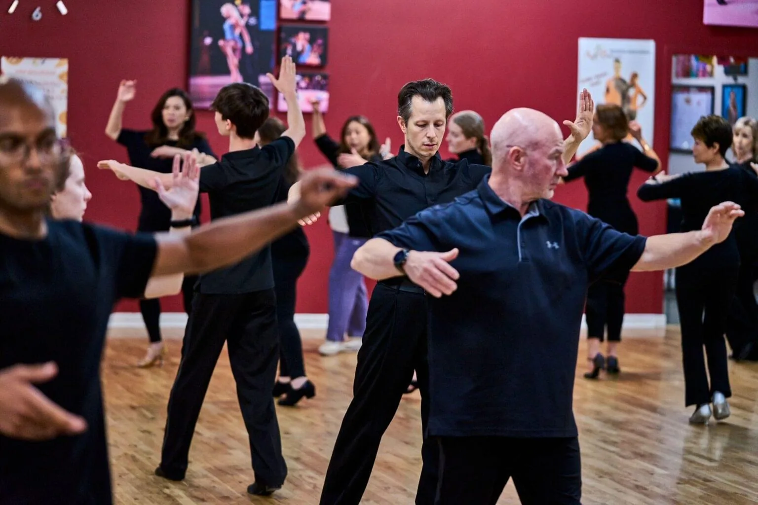 Group of dancers moving together on the wood floor at Aria Ballroom, red walls lined with performance photos, salsa, bachata venue in Seattle