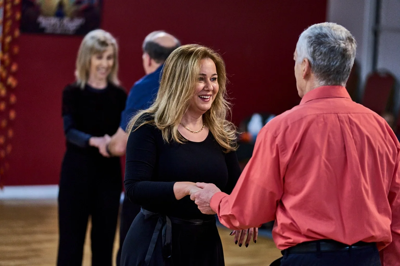 Dancers greeting each other on the floor at Aria Ballroom, red walls and other couples in the background