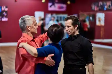 Instructor guiding a couple in a dance hold at Aria Ballroom, red walls with framed dance photos, salsa, bachata venue in Seattle