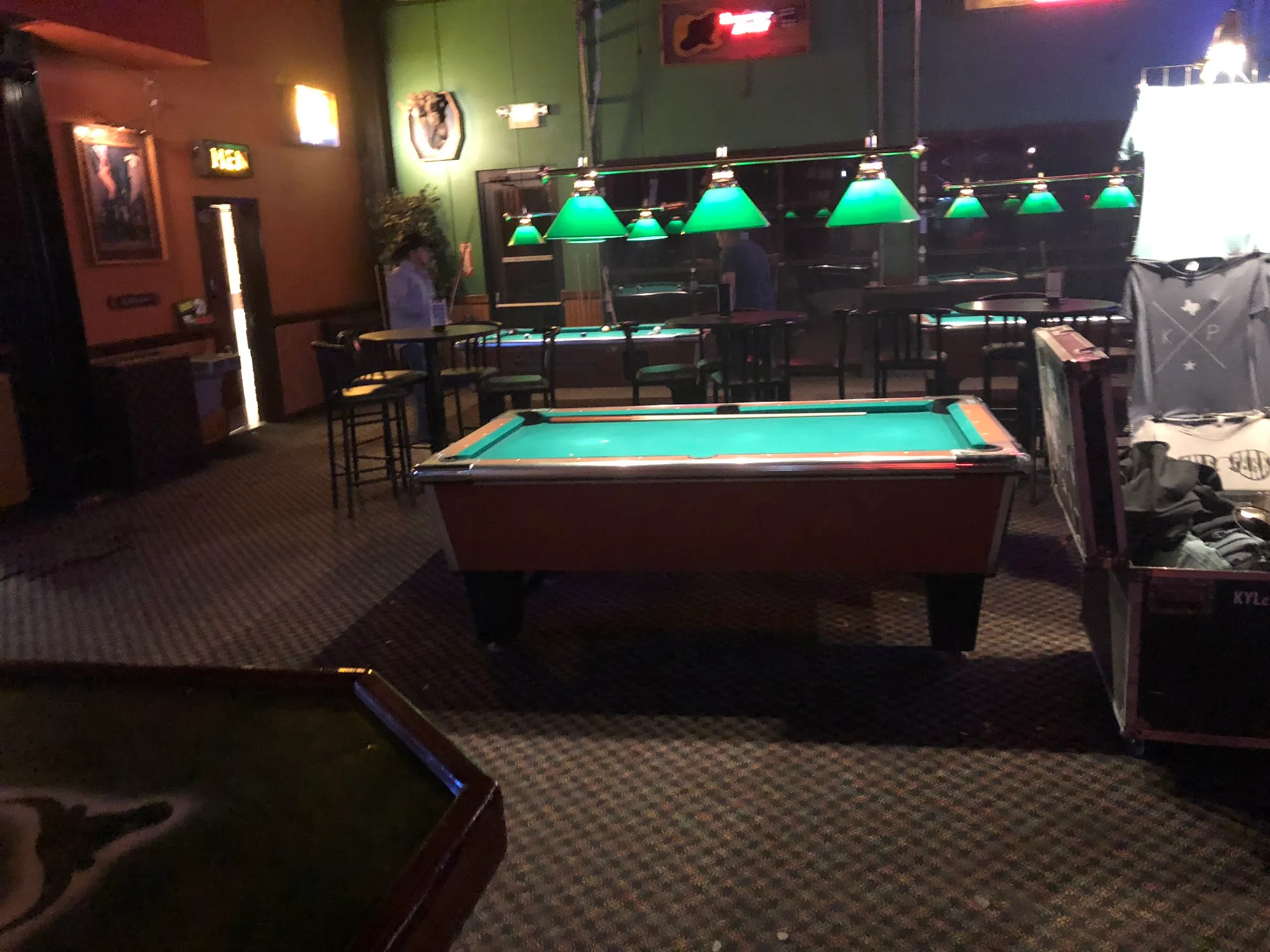 Pool tables under green lamps in the game-room lounge at Wild West Cedar Park