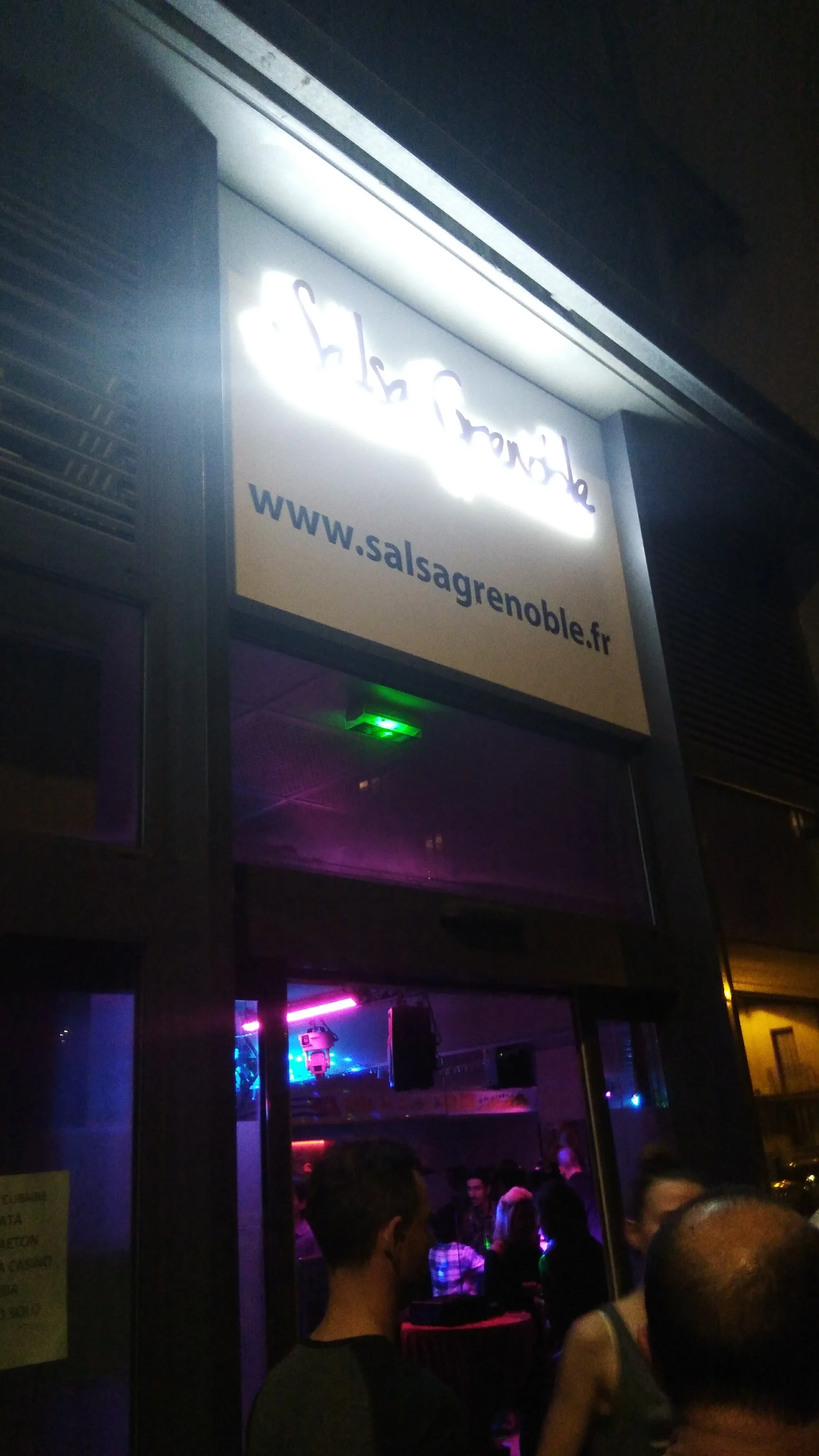 Salsa Grenoble entrance at night with lit sign and crowd entering the venue