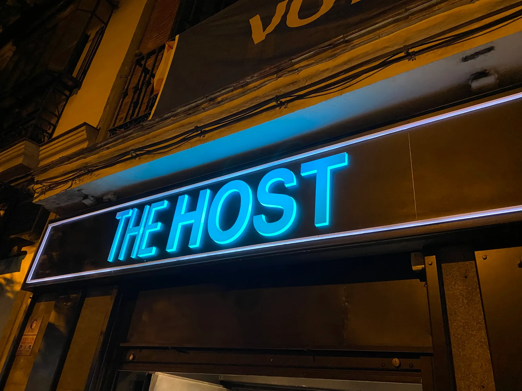Neon sign for The Host nightclub glowing blue outside in Madrid