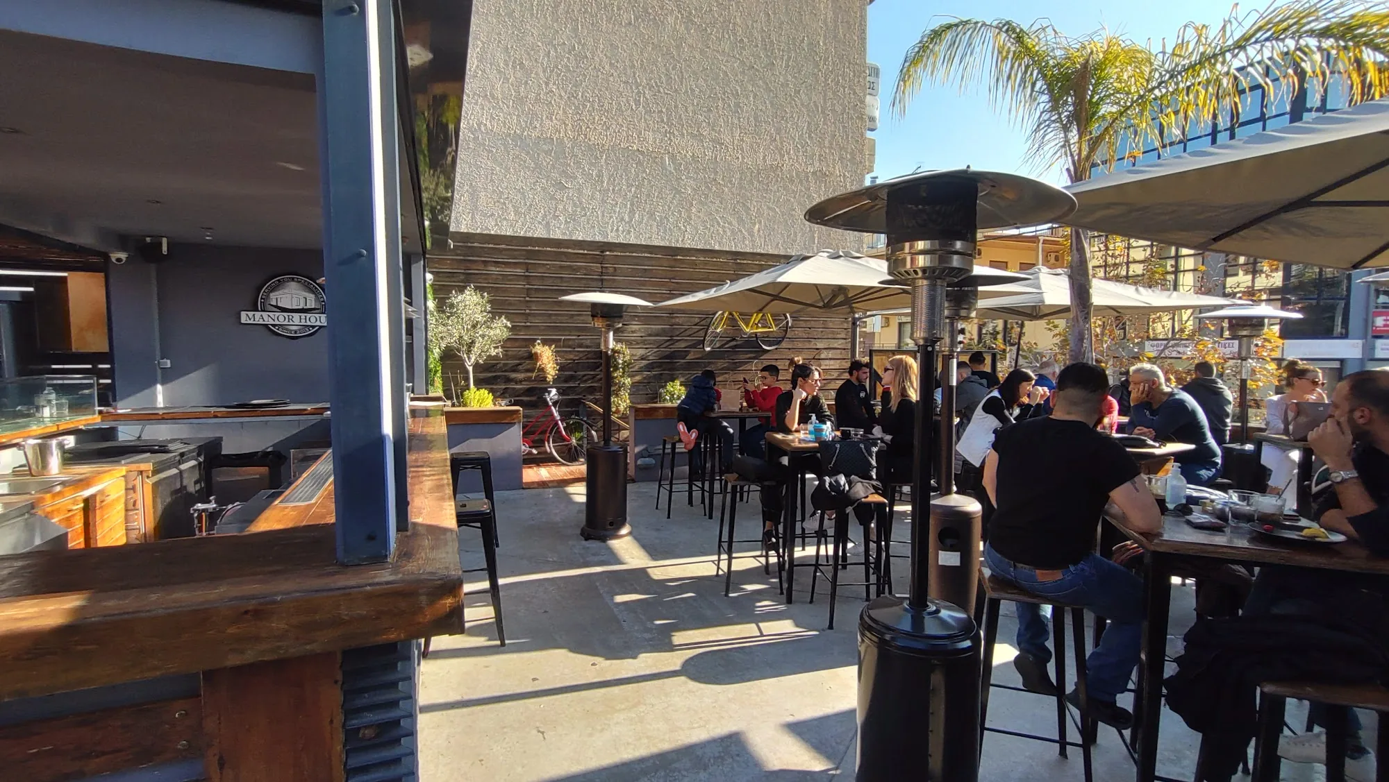 Manor House Athens sunny outdoor patio with guests and Manor House signage in background