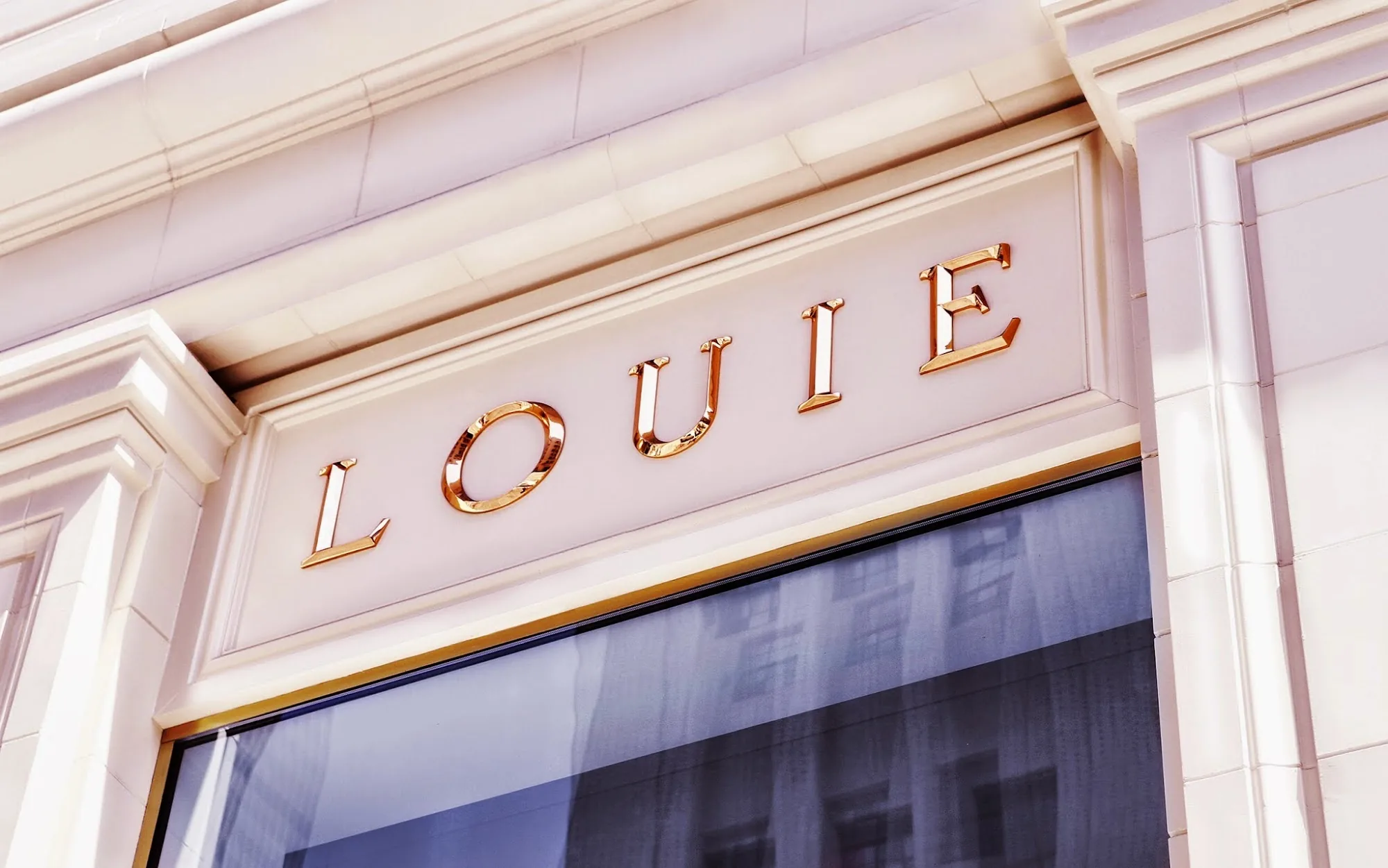 Louie exterior signage with gold letters on a cream stone facade in Los Angeles