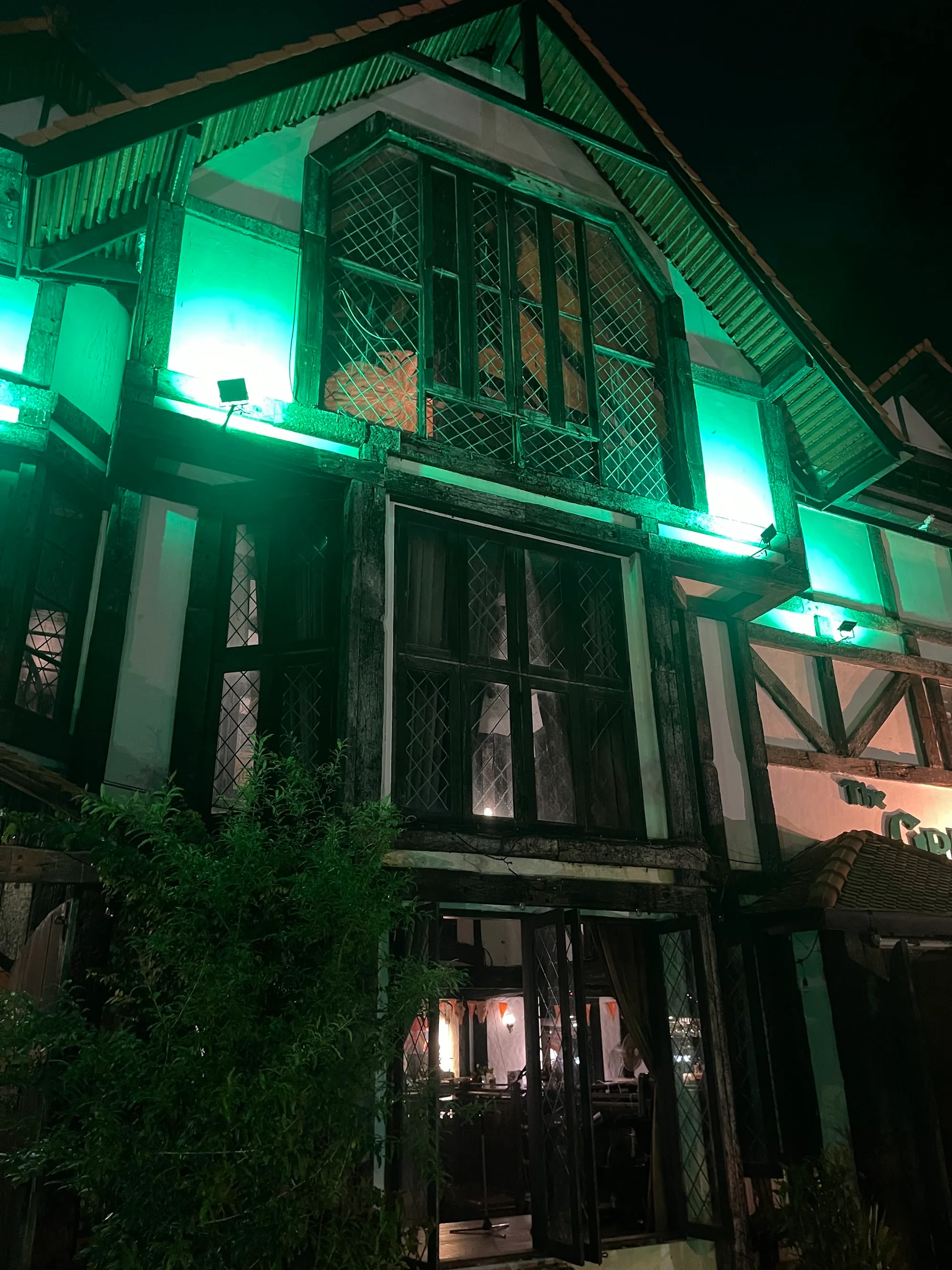The Green Man pub in Phuket lit up at night with green floodlights on its Tudor facade