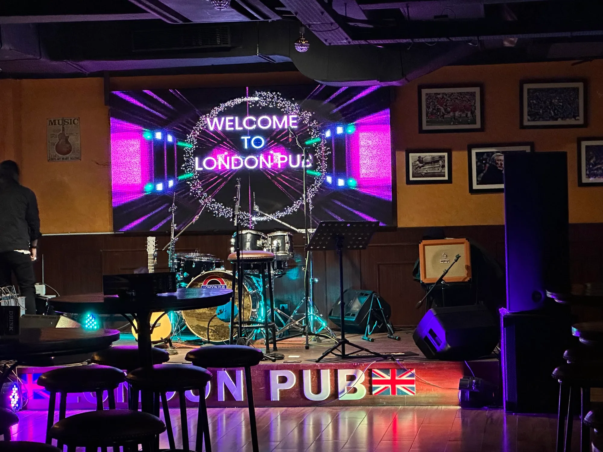 Welcome to London Pub LED screen on stage with live band setup and London Pub signage