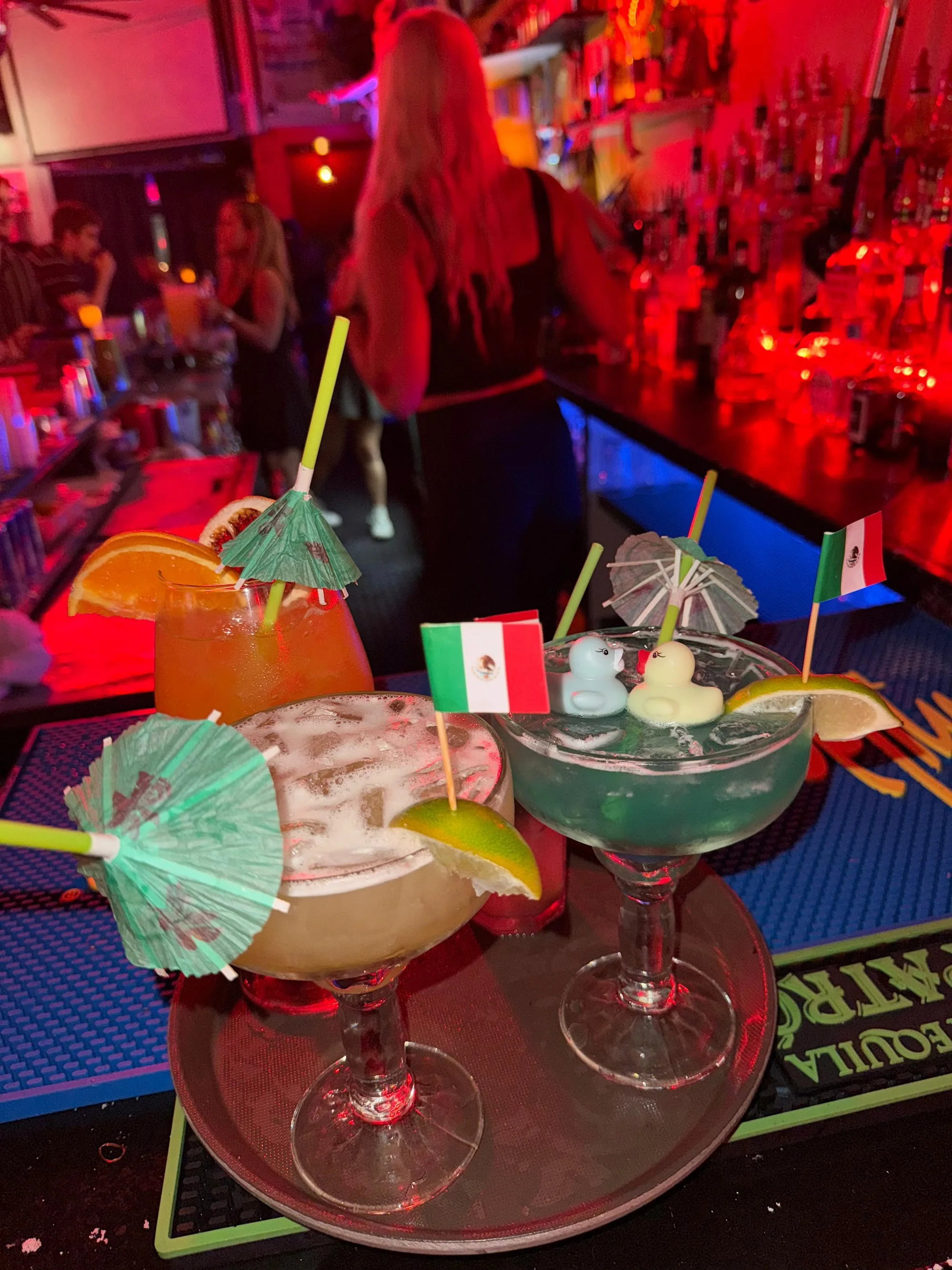Tray of cocktails at the bar amid red party lighting and crowd at Cafe Citron in Washington, D.C.