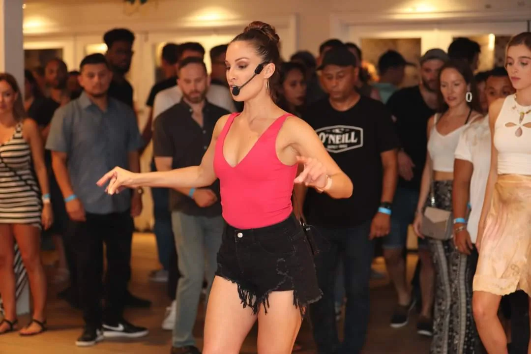 Bachata dance instructor leading a class at The Continental Club in Los Angeles, demonstrating moves to a crowd of students on the dance floor