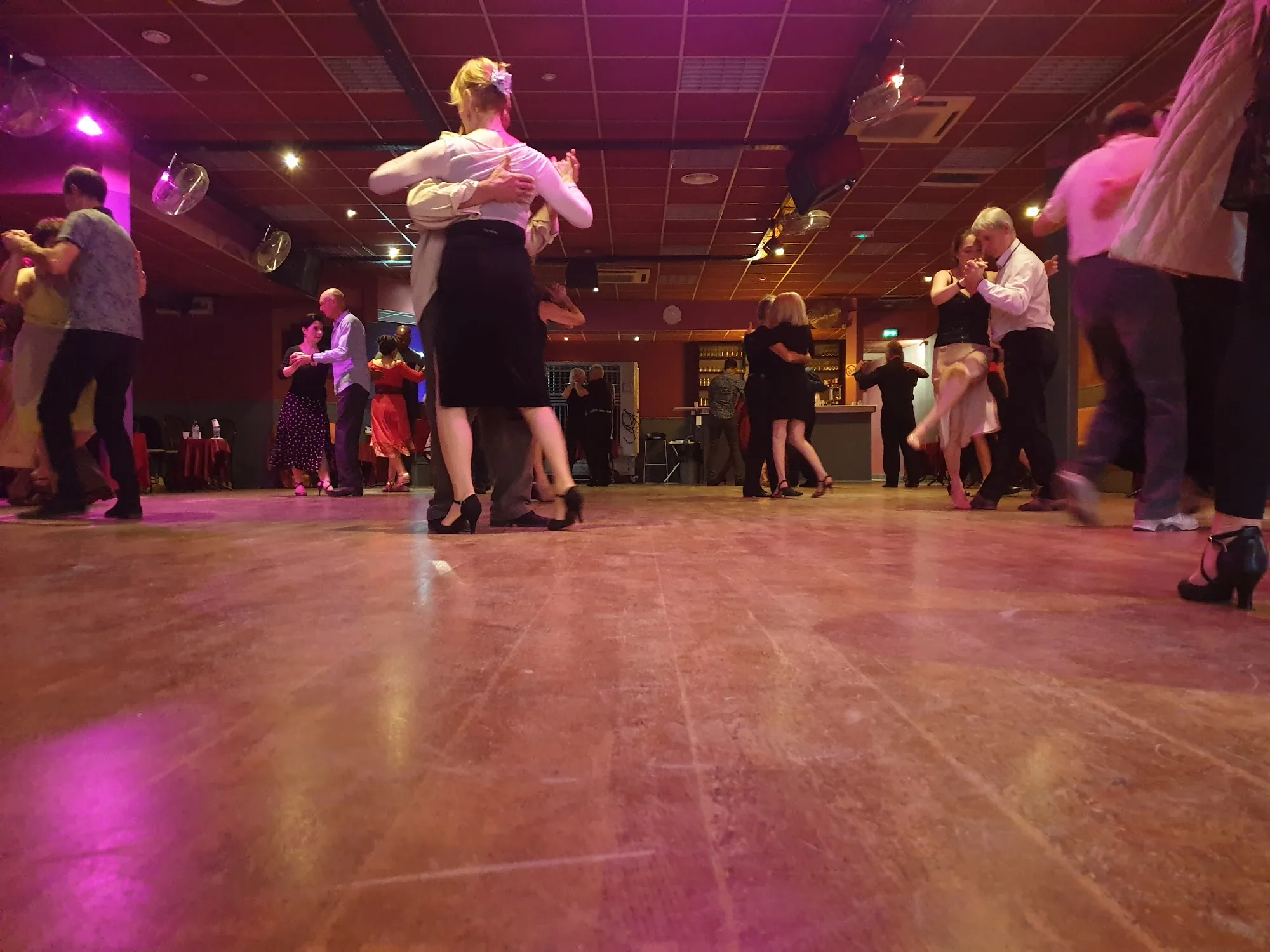 Couples social dancing on the wooden dance floor at Sensation Dance School in Paris under warm stage lighting