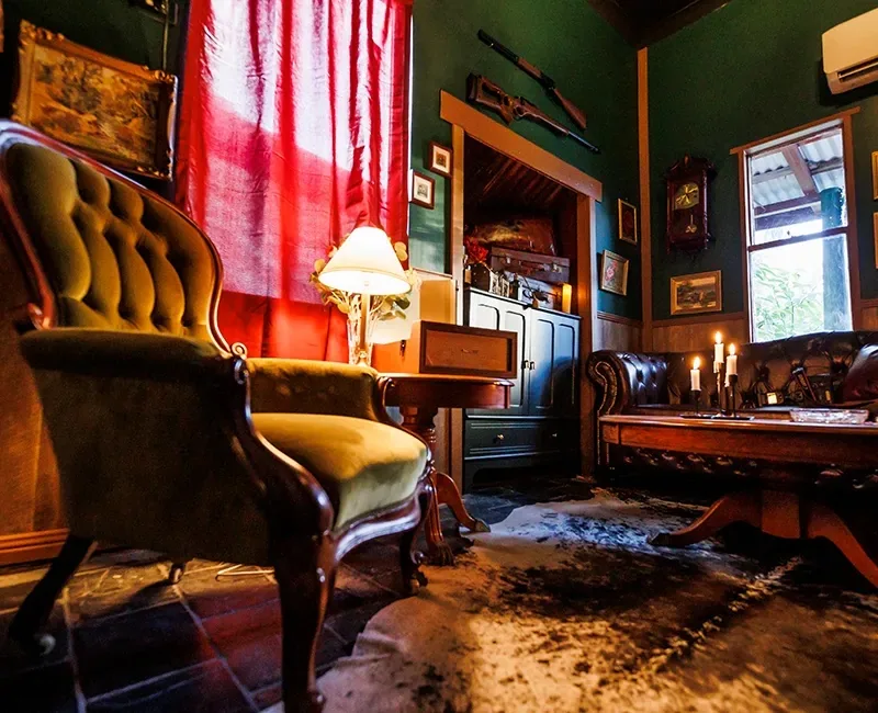 Vintage-styled interior lounge with deep green walls, tufted velvet armchairs, a red curtain and antique furnishings at The Fourth Monkey Cocktail Bar & Grill, Brisbane.