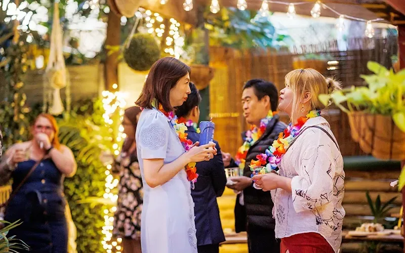 Guests wearing colourful leis chatting in the fairy-lit tropical garden area during an event at The Fourth Monkey Cocktail Bar & Grill, Brisbane.