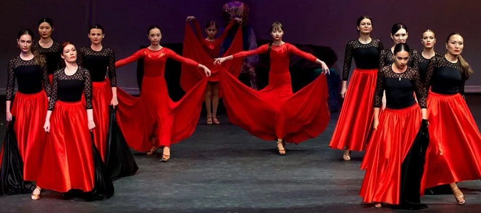 Dancers in red skirts and black tops performing a Spanish-style group routine on stage at LaVida Dance Studio, Seattle.
