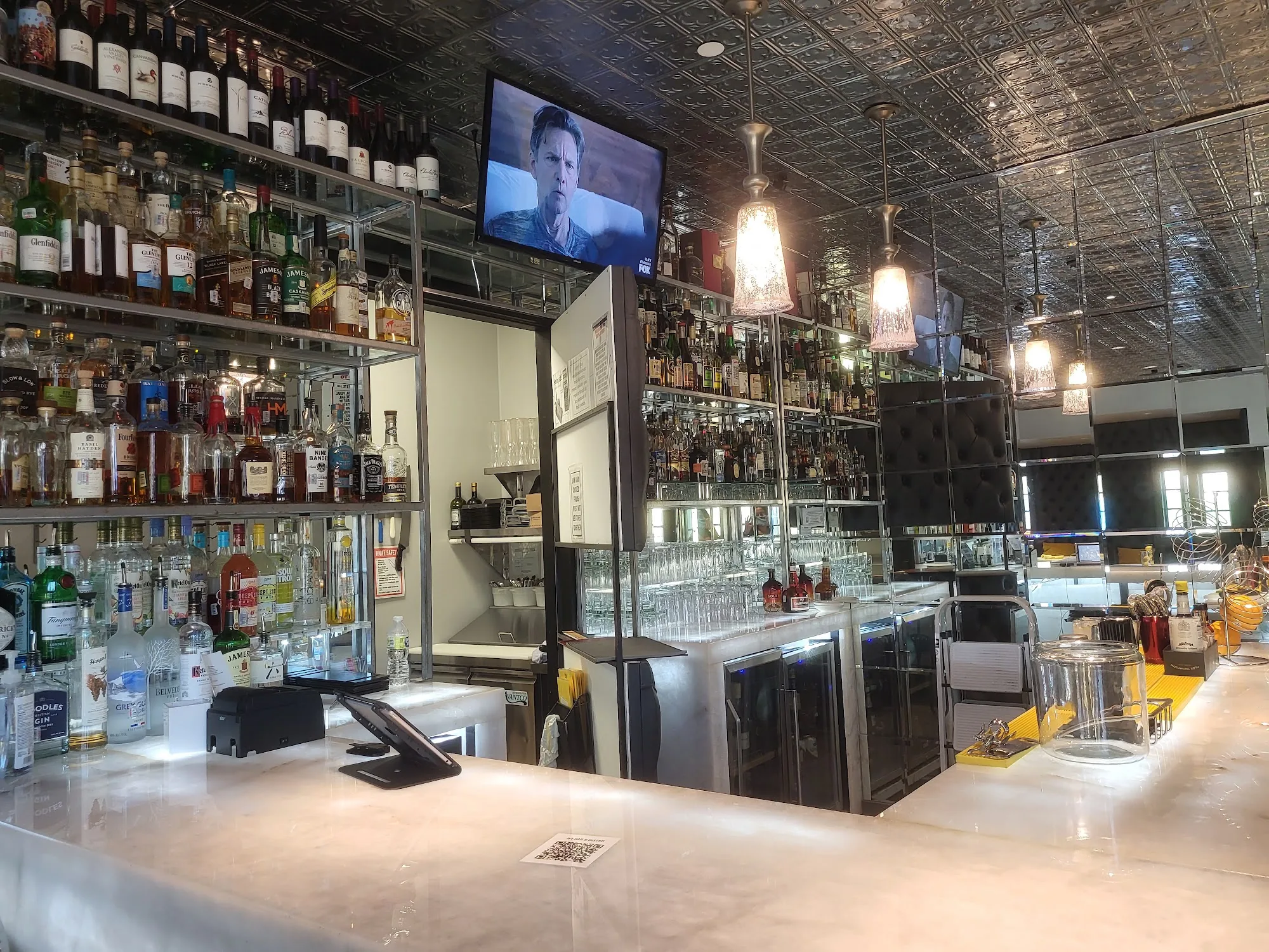 Long marble bar with full liquor shelves and tin ceiling at Ivy Bar & Bistro, Houston