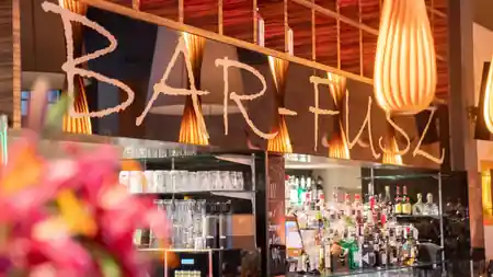Bar counter with BAR-FUSZ branded sign and warm orange lighting at Barfusz Leipzig — salsa, bachata venue in Leipzig