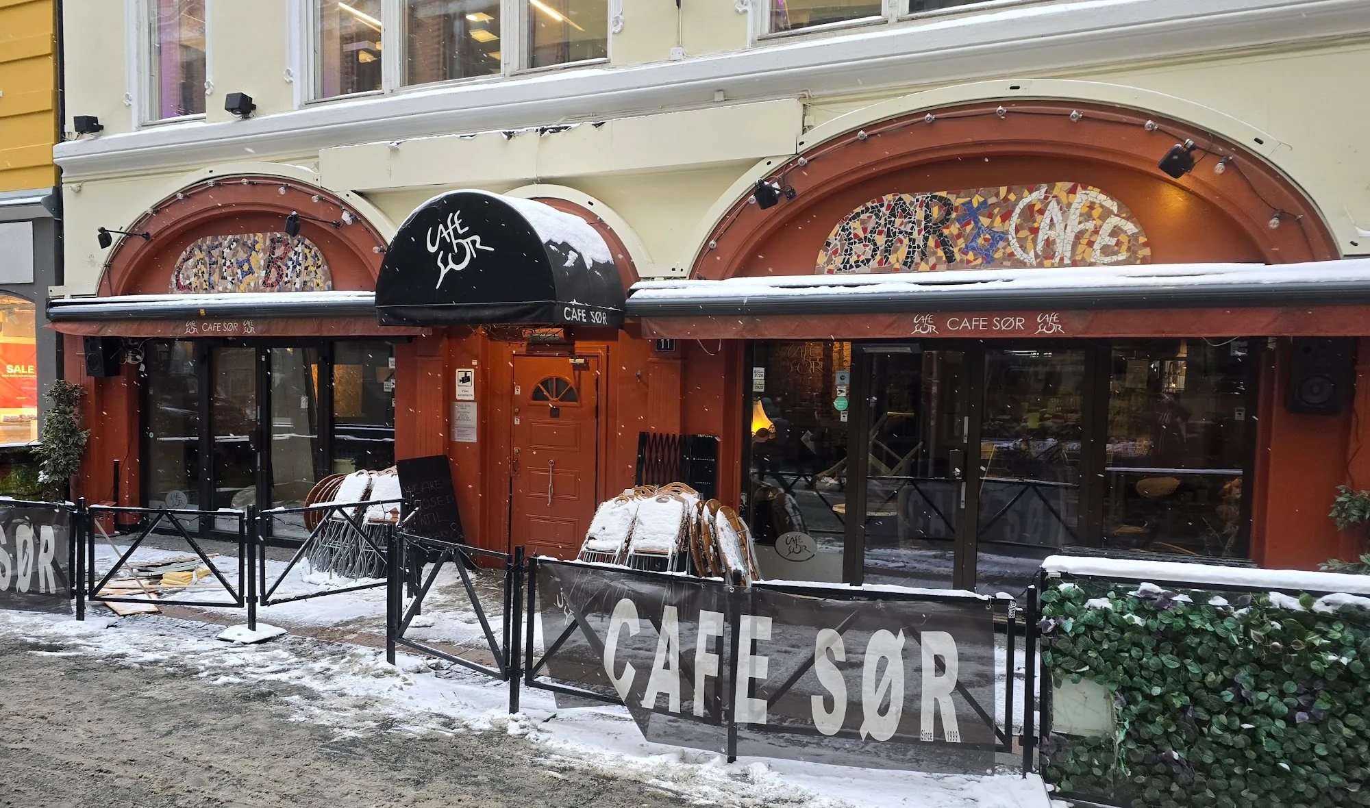 Snow-covered street exterior of Cafe Sor with CAFE SOR signage in Oslo