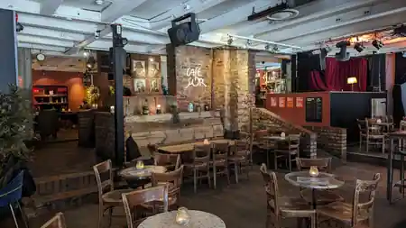 Interior of Cafe Sor with brick stage backdrop, bar and clustered tables, salsa, bachata venue in Oslo
