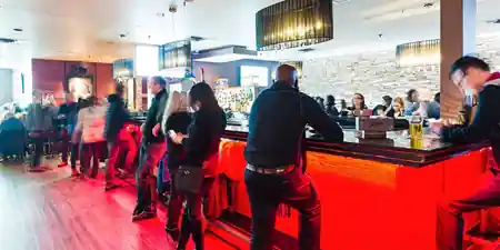 Busy bar and lounge interior at Smokeshow BBQ and Brew Toronto with people gathered along the counter under red accent lighting, bachata venue in Toronto