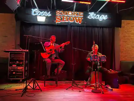 Two musicians performing on the neon-lit Smoke Show stage inside Smokeshow BBQ and Brew Toronto, bachata venue in Toronto