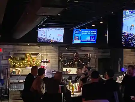 Crowd gathered at the bar of Smokeshow BBQ and Brew Toronto with big screens and string lights overhead, bachata venue in Toronto