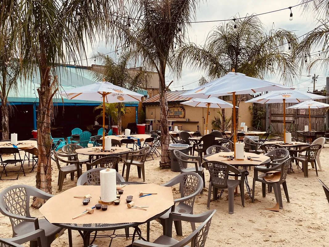 Outdoor sand-floored patio with palm trees, white umbrellas, and casual table seating at The Original Cancun Cantina, Hanover.