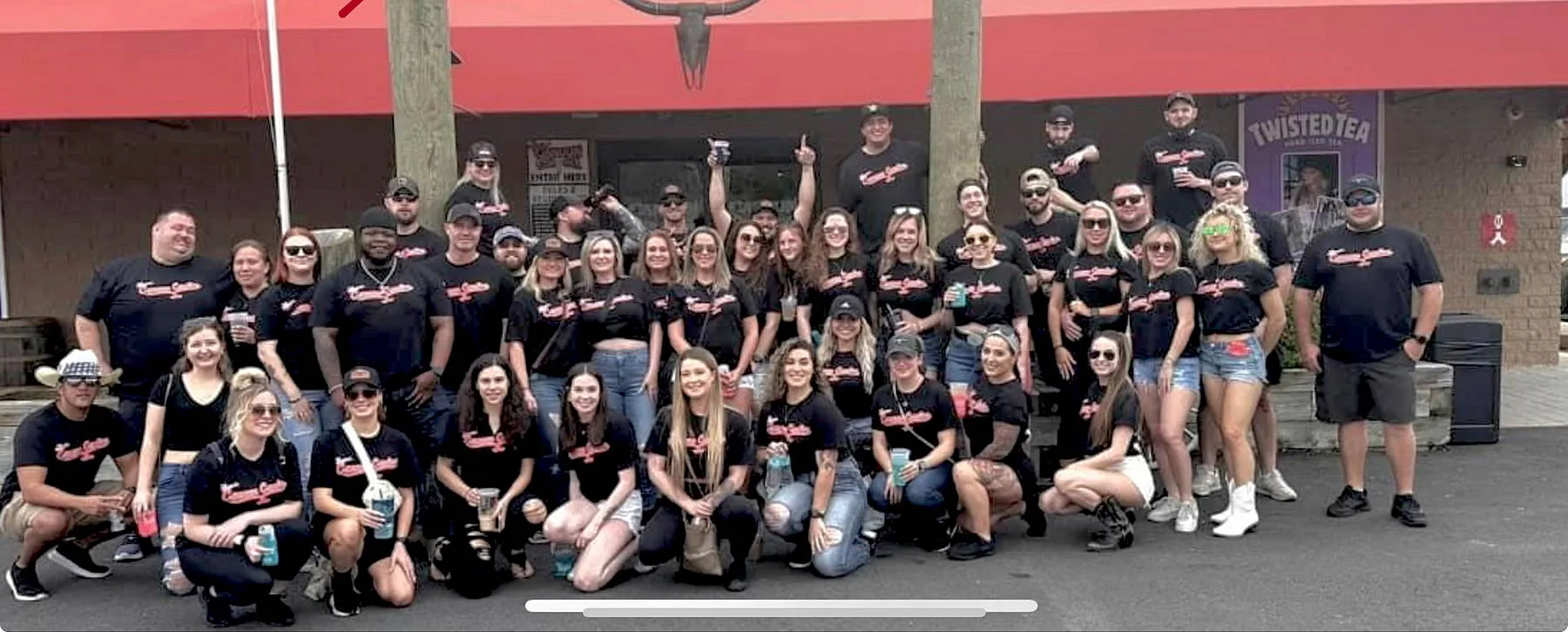 Large group of staff and patrons in matching t-shirts posed outside the red-awning entrance of The Original Cancun Cantina, Hanover.