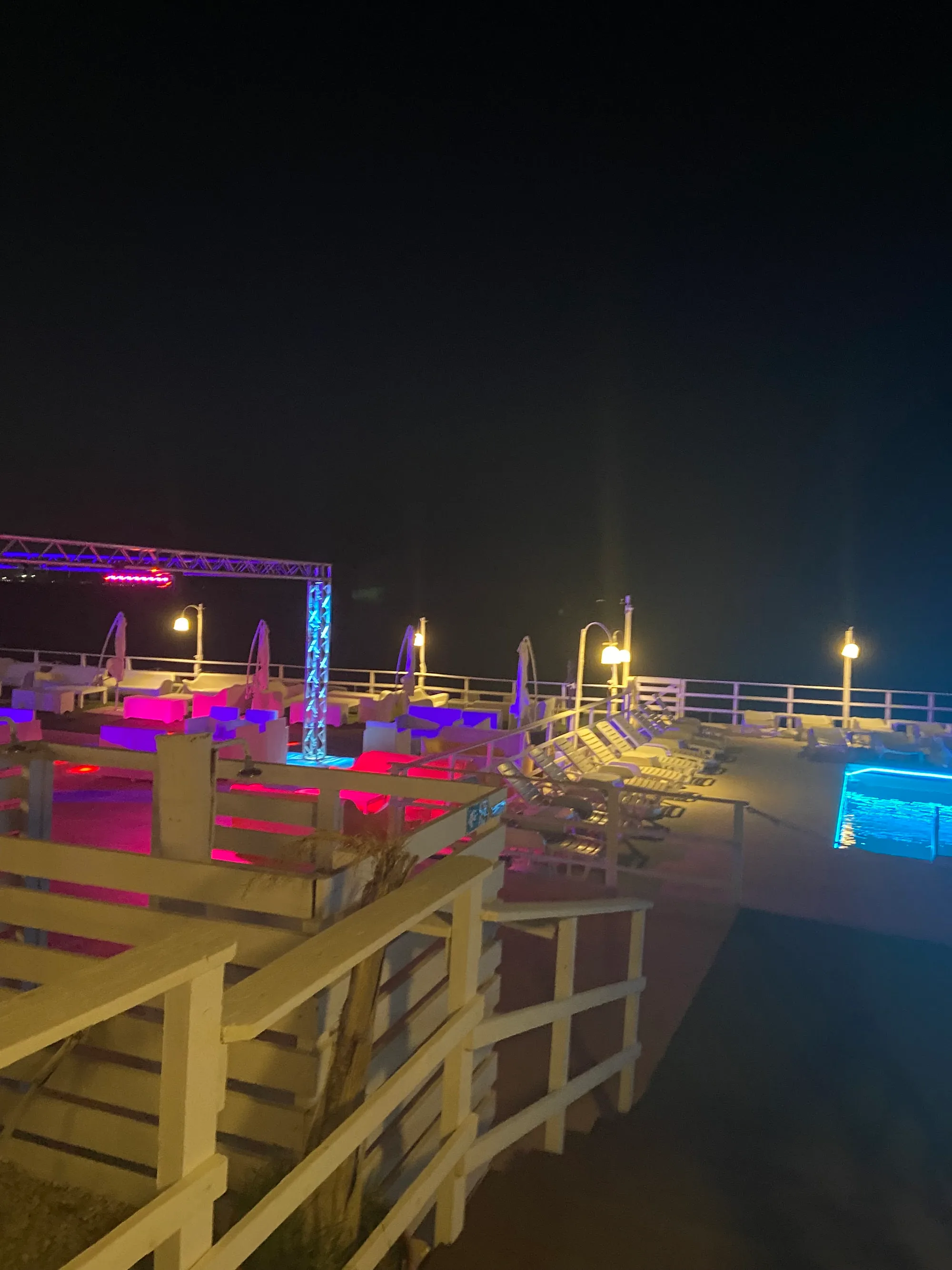 Beachfront stage truss and neon-lit terrace at Sea Public in Aspra, Italy
