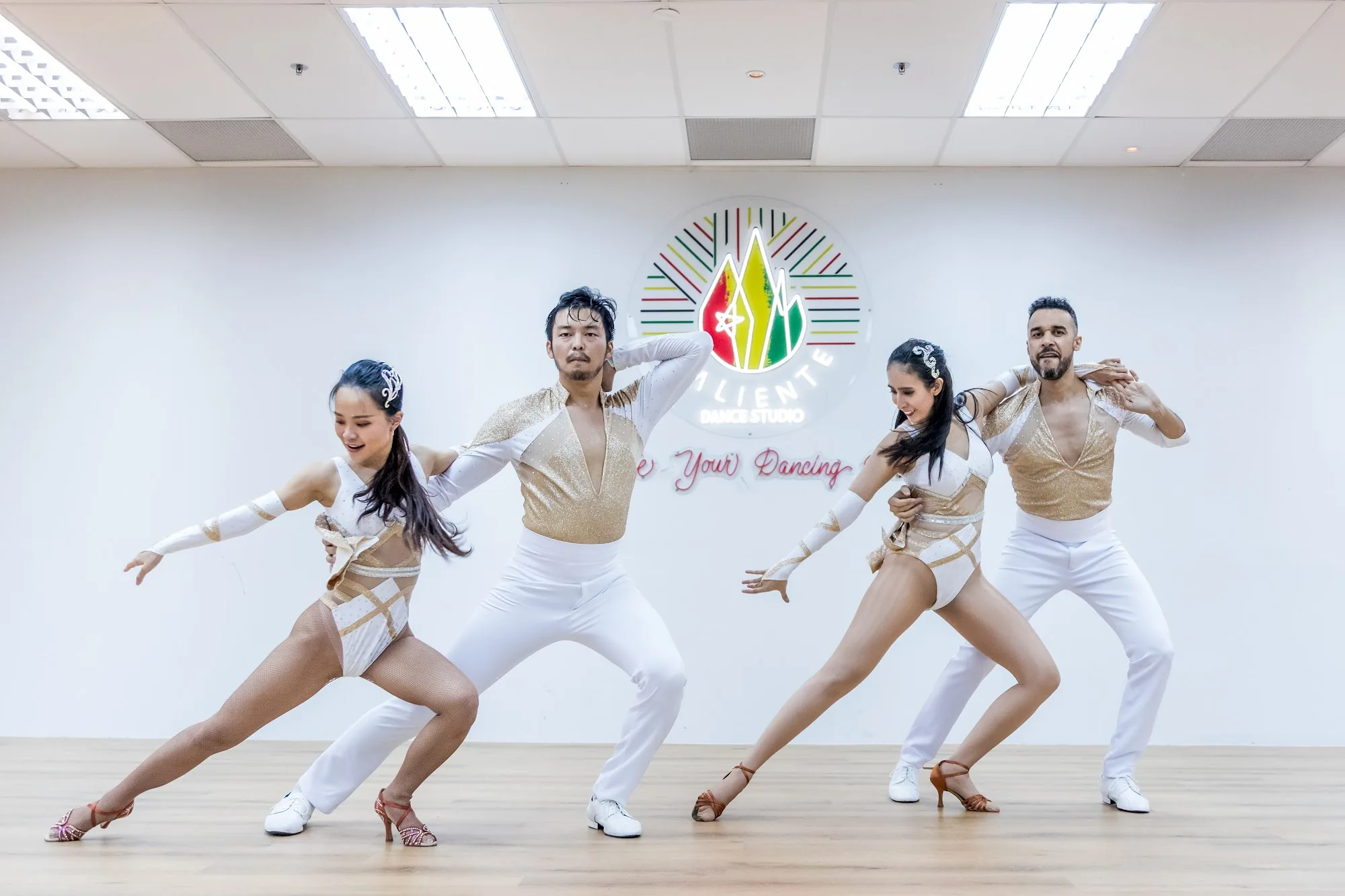 Latin dance troupe posing in front of Caliente Dance Studio neon sign Singapore