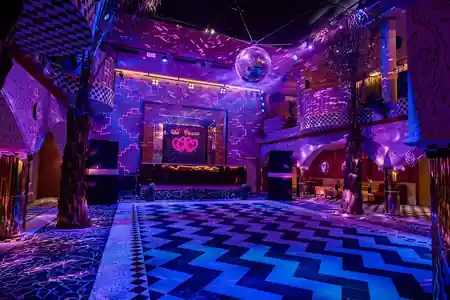 Club Corazon Bali's dramatic empty dance floor with zigzag tile pattern, mirror ball, purple club lighting, and neon Club Corazon sign — bachata venue in Bali