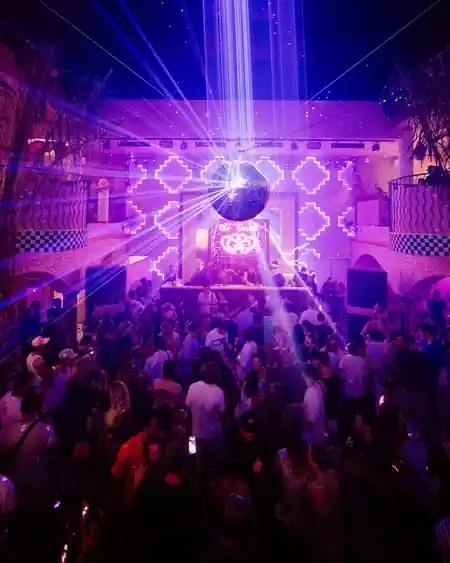 Packed dance floor at Club Corazon Bali with crowd of dancers, DJ booth, mirror disco ball, and purple laser light show — bachata venue in Bali