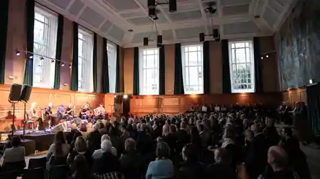 Kennedy Hall interior at Cecil Sharp House, London showing a live music performance with seated audience in the grand wood-paneled hall — salsa, bachata venue in London