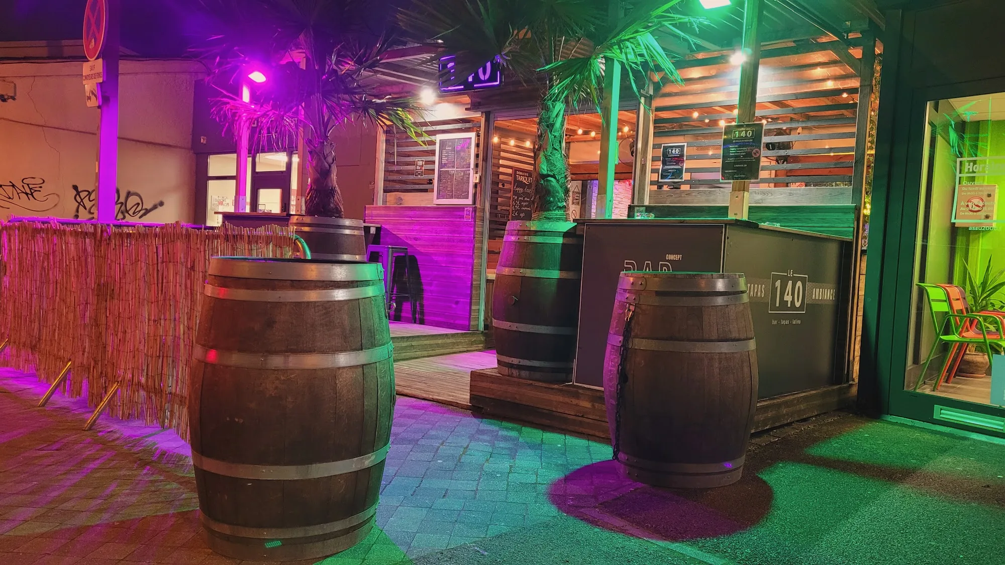 Outdoor terrace of Le 140 Bar with barrels and 140 signage lit in neon green and pink