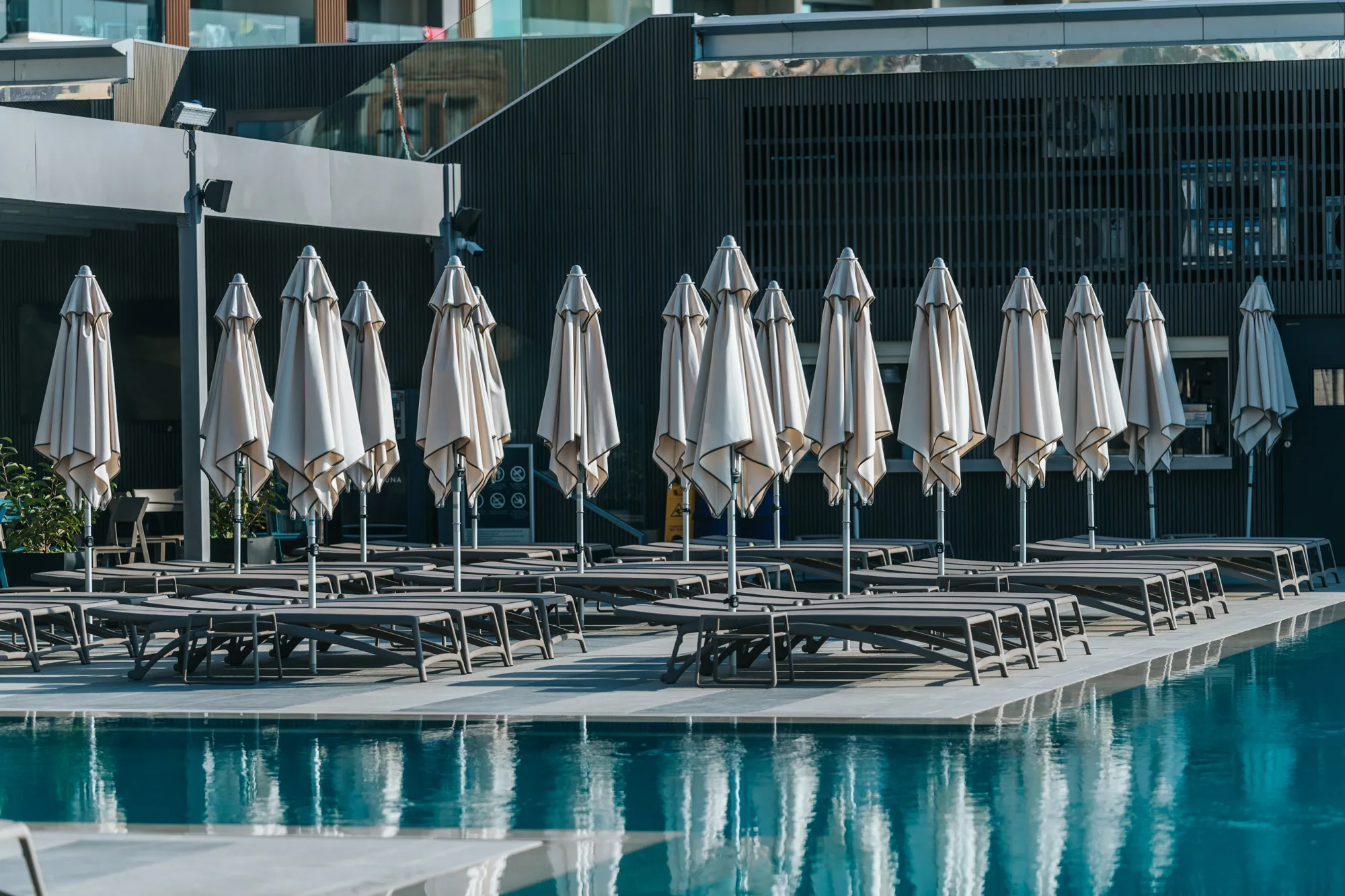 Poolside deck with rows of grey sun loungers and closed parasols beside the pool at Aqualuna Beach Club, Malta