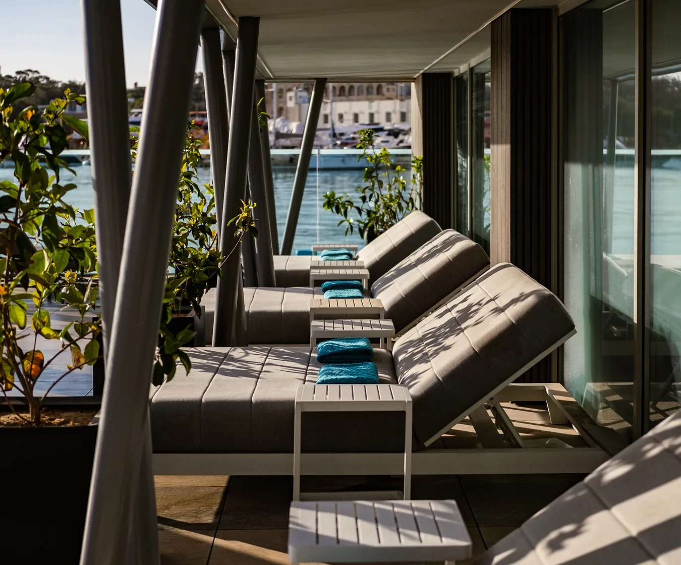 Row of cushioned cabana daybeds with towels and a marina view beside the pool at Aqualuna Beach Club, Malta