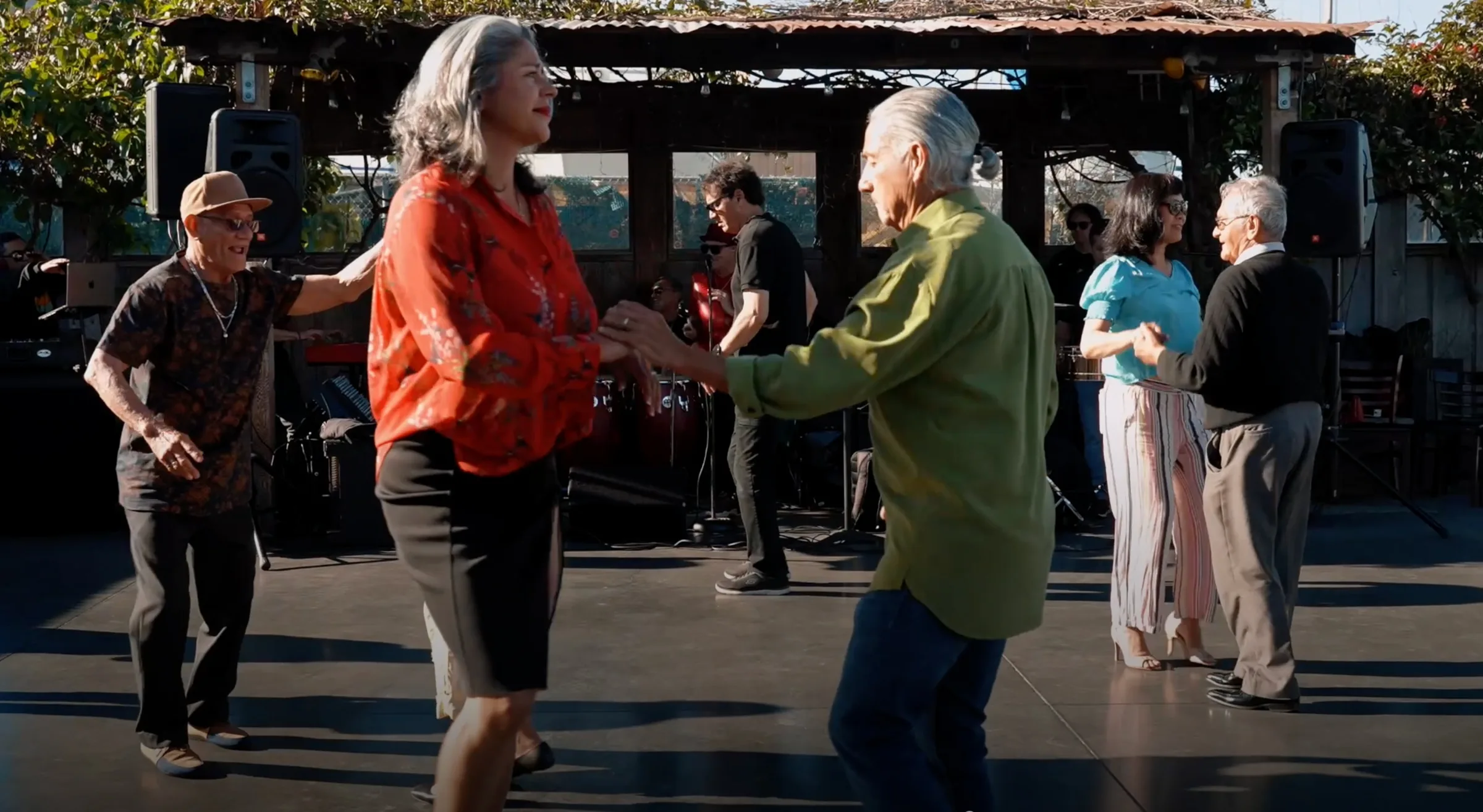 Couples dancing outdoors on the waterfront patio in front of a live Latin band playing congas and accordion under a wooden gazebo at The Ramp Restaurant, San Francisco.