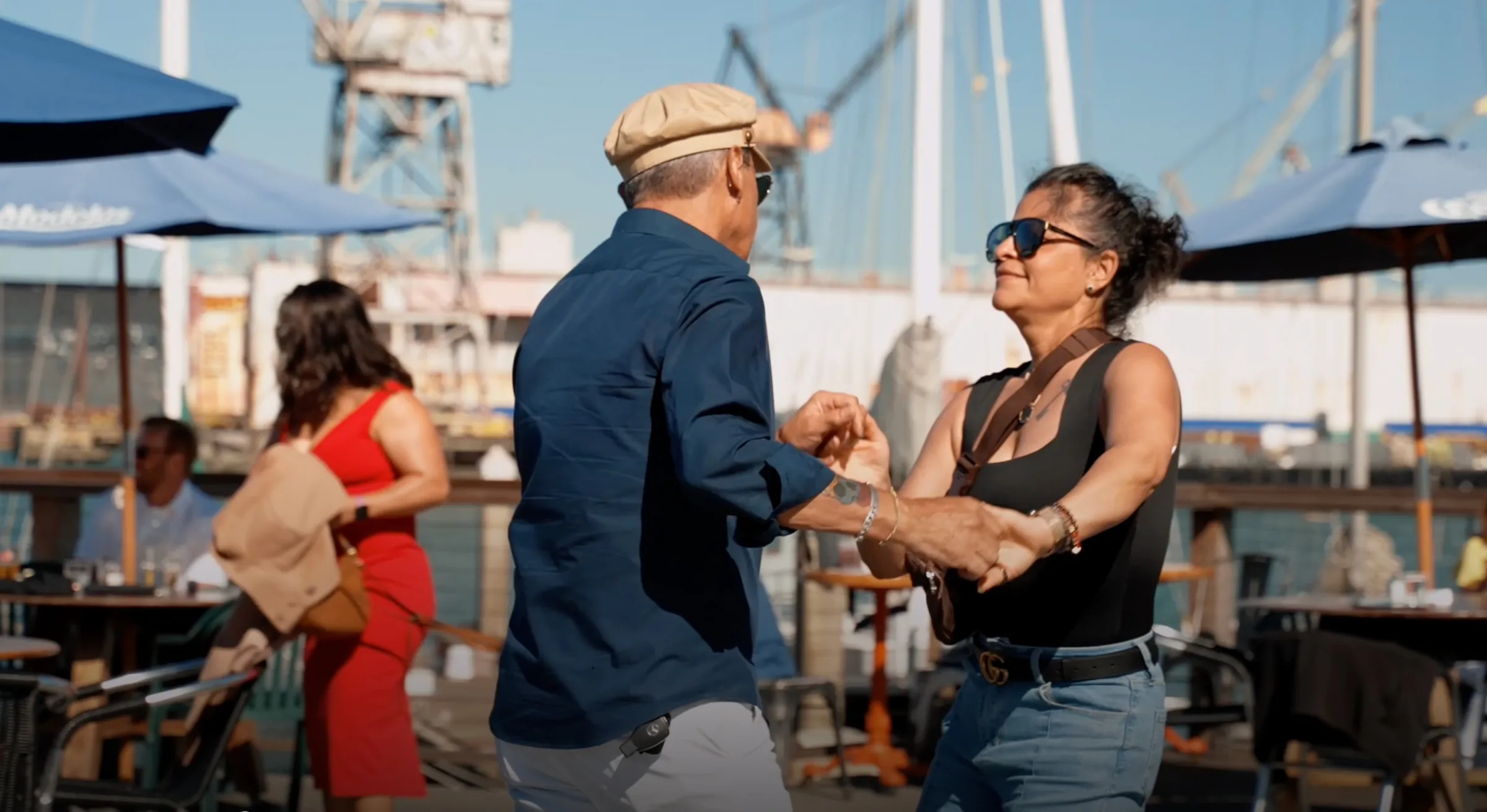 Two couples dancing on the open-air waterfront deck with shipyard cranes and boat masts in the background at The Ramp Restaurant, San Francisco.